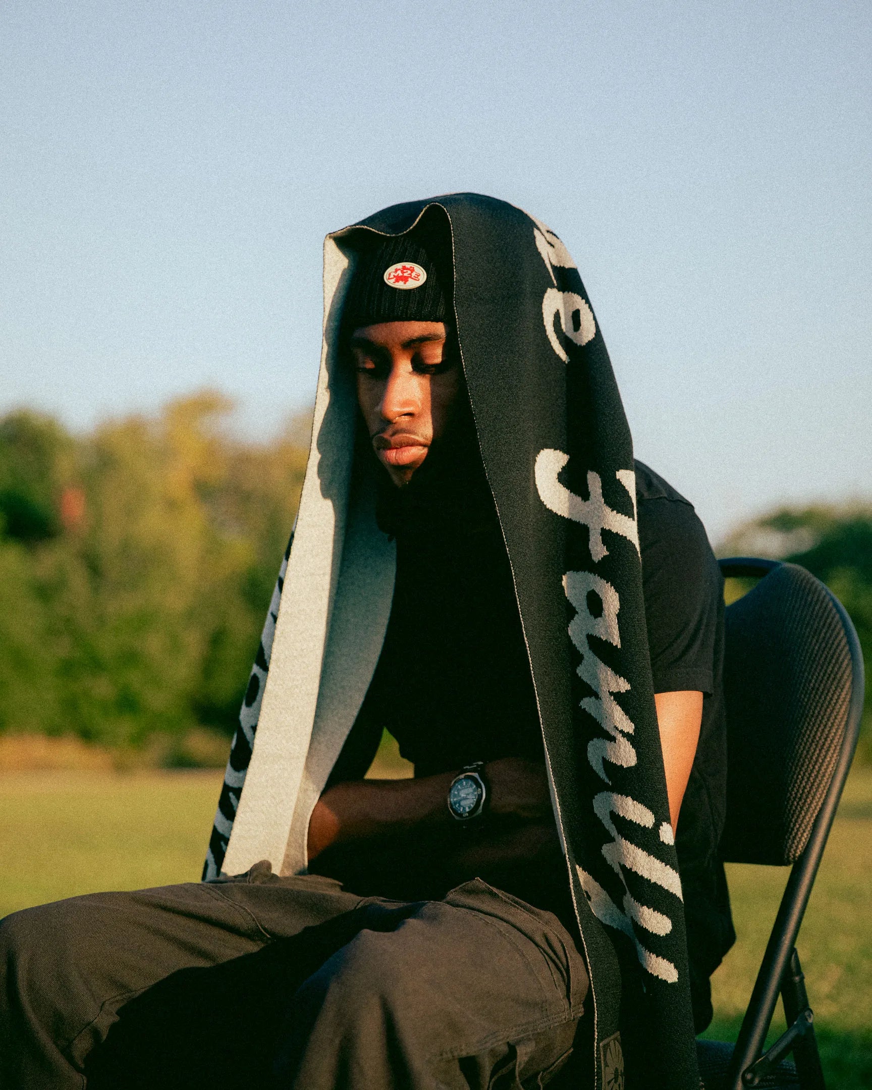 Person sitting outdoors with a large black and white M2E scarf draped over their shoulders.