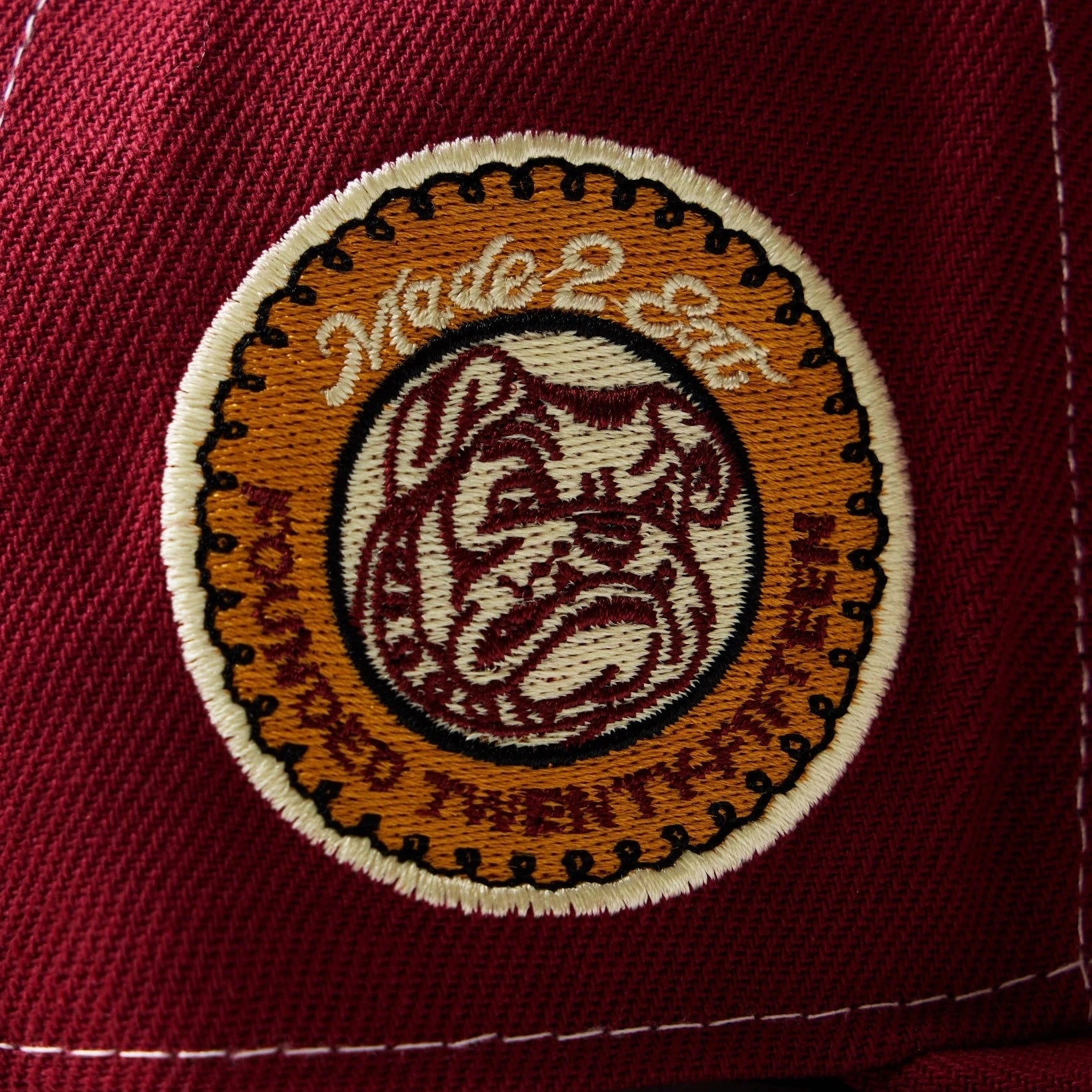 Close-up of a maroon cap with an embroidered logo on a white background