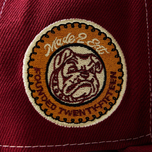 Close-up of a maroon cap with an embroidered logo on a white background