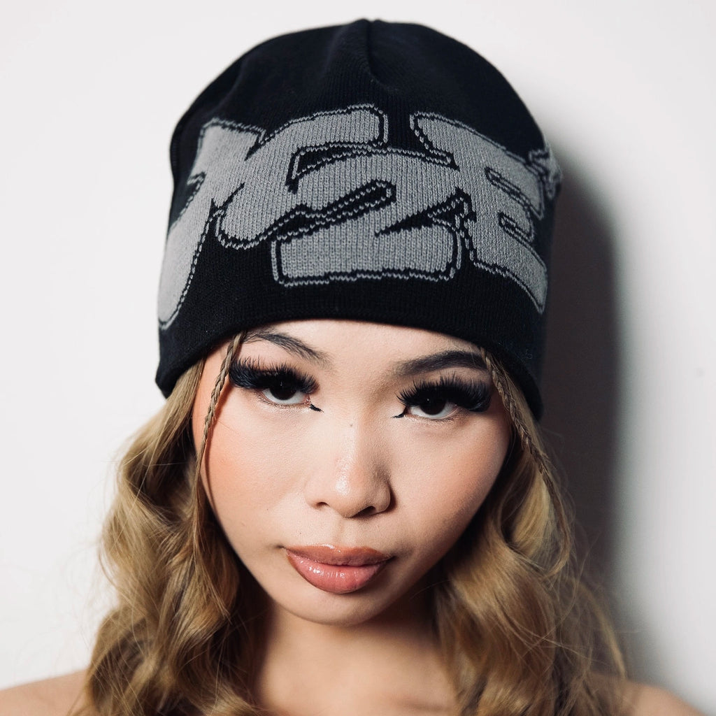 Woman wearing a black M2E beanie with a logo on a plain background