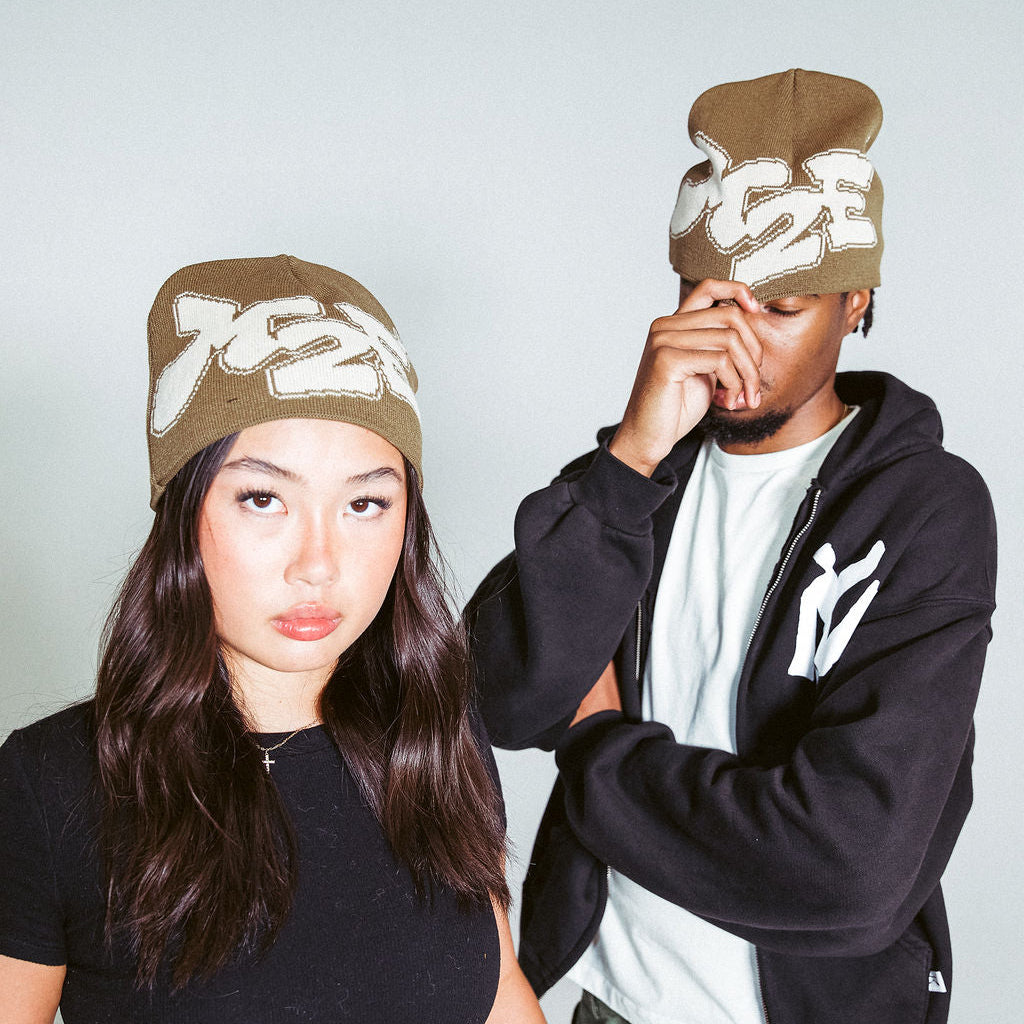 Two people wearing brown M2E beanies with logos against a plain background