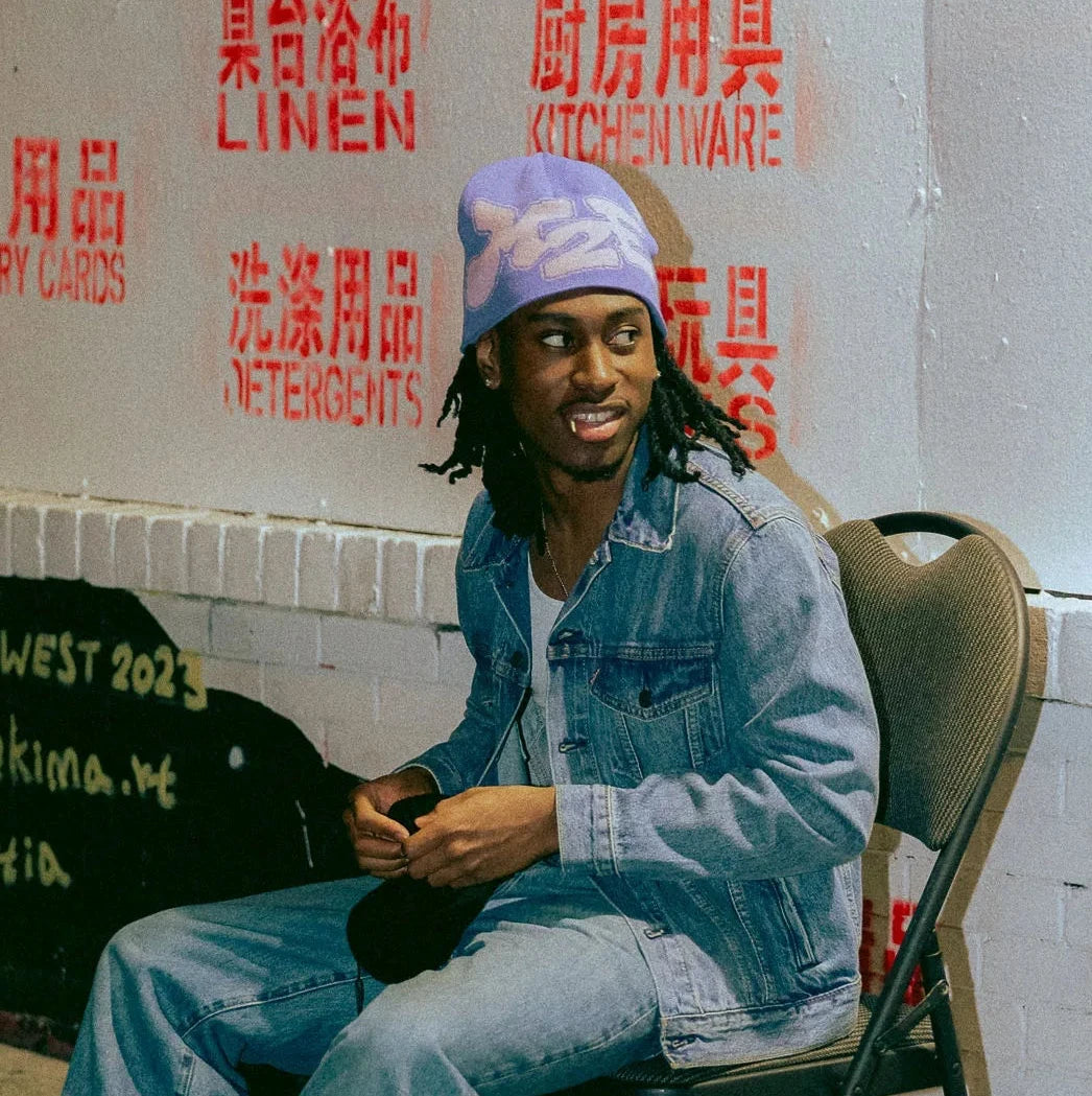Person sitting in a jean jacket wearing a lilac M2E beanie