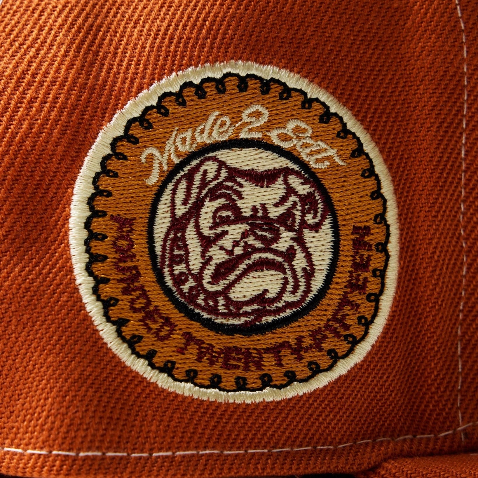 Close-up of a orange fitted cap with a embroidered bulldog logo on a white background