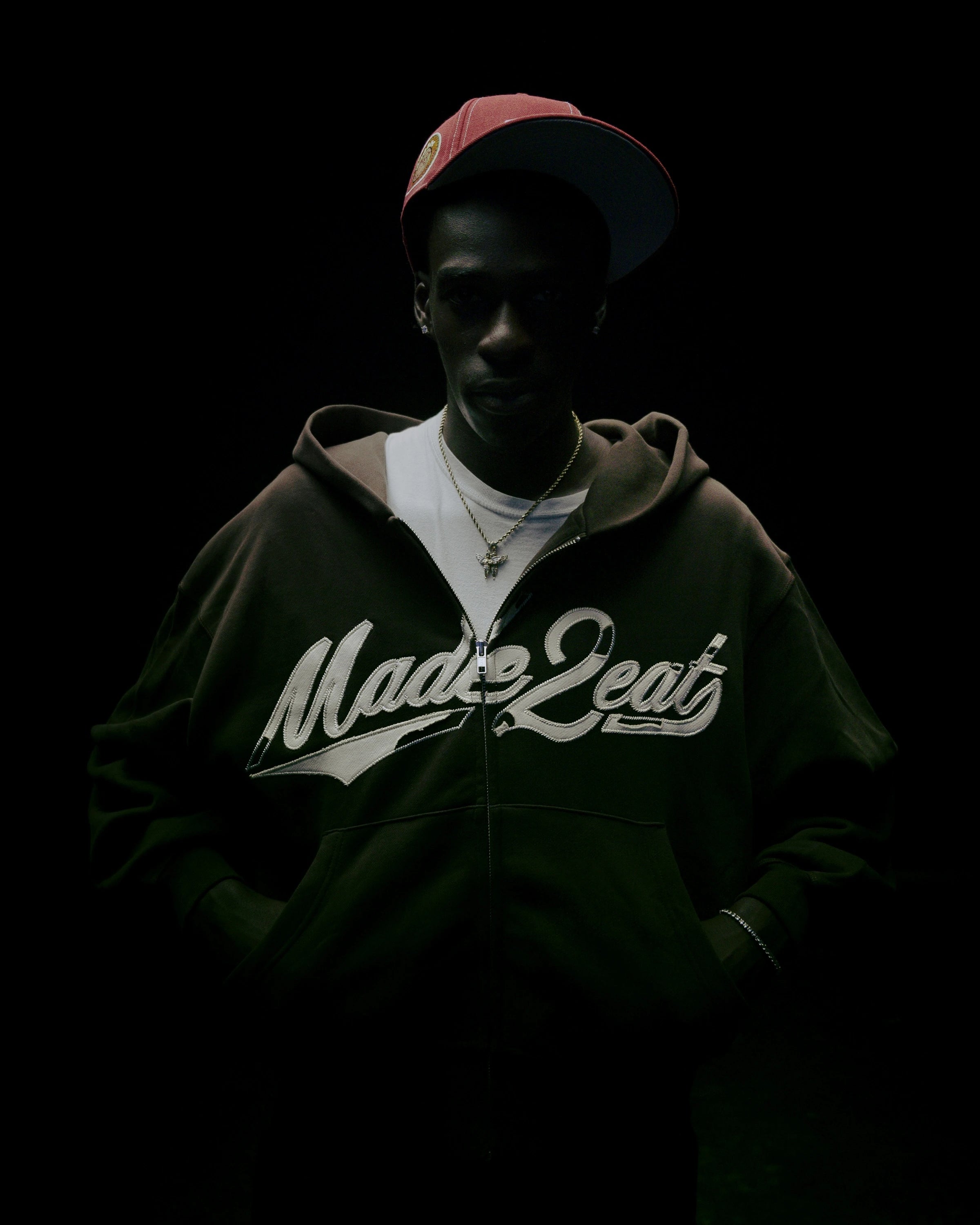 a figure standing in a spotlight with a brown hoodie that says "made2eat" stitched across the chest.