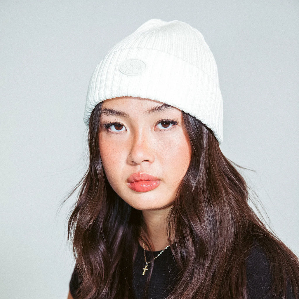 Woman wearing a cream M2E skully beanie against a grey background